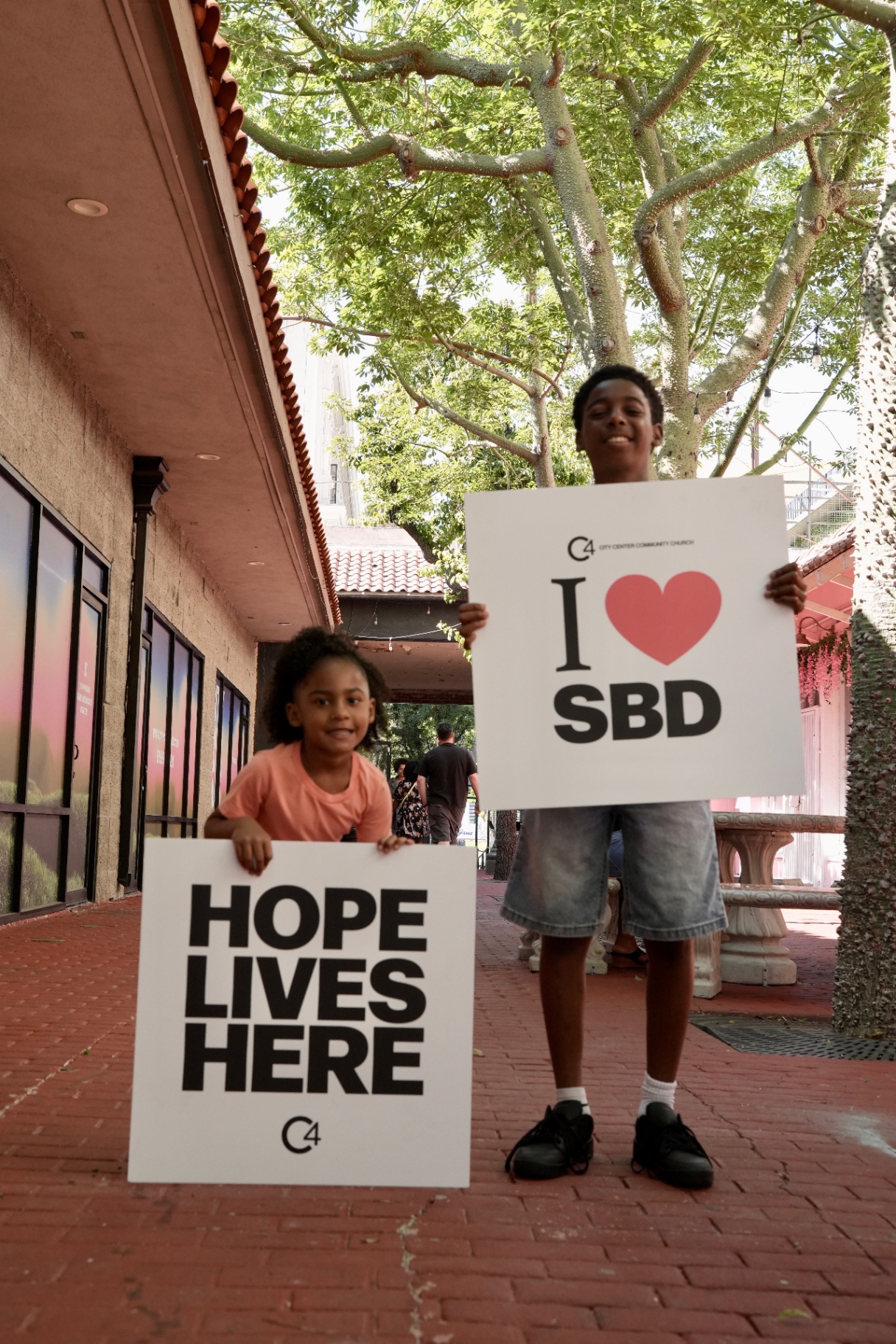 Two kids holding 'Hope Lives Here' and 'I love SBD' signs in downtown San Bernardino