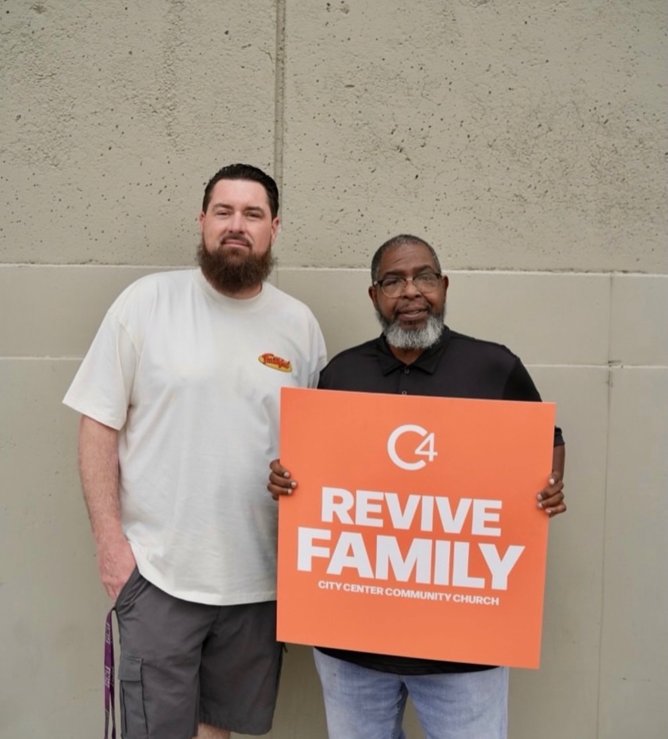 Two men holding a C4 'Revive Family' sign outside the church